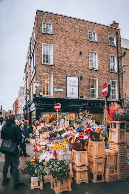 A bustling flower market on Marylebone High Street, featuring an array of vibrant fresh flower bouquets and floral arrangements displayed on wooden crates outside a shop named MRS, which specializes i